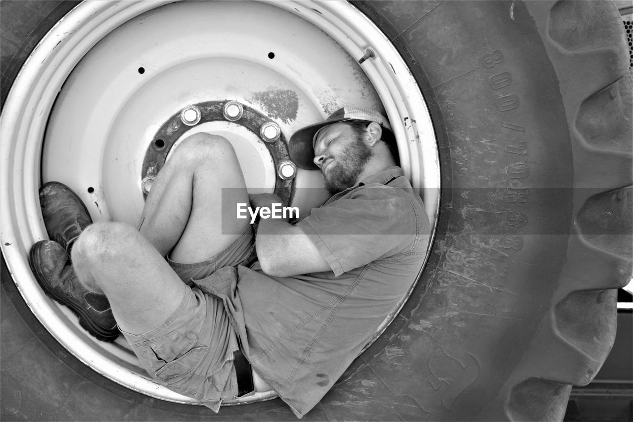 Side view of man sleeping on tire
