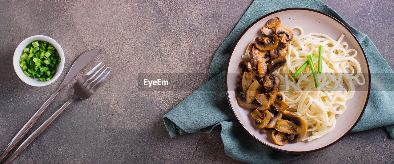 Udon noodles, fried champignons and greens on a plate on the table top view web banner