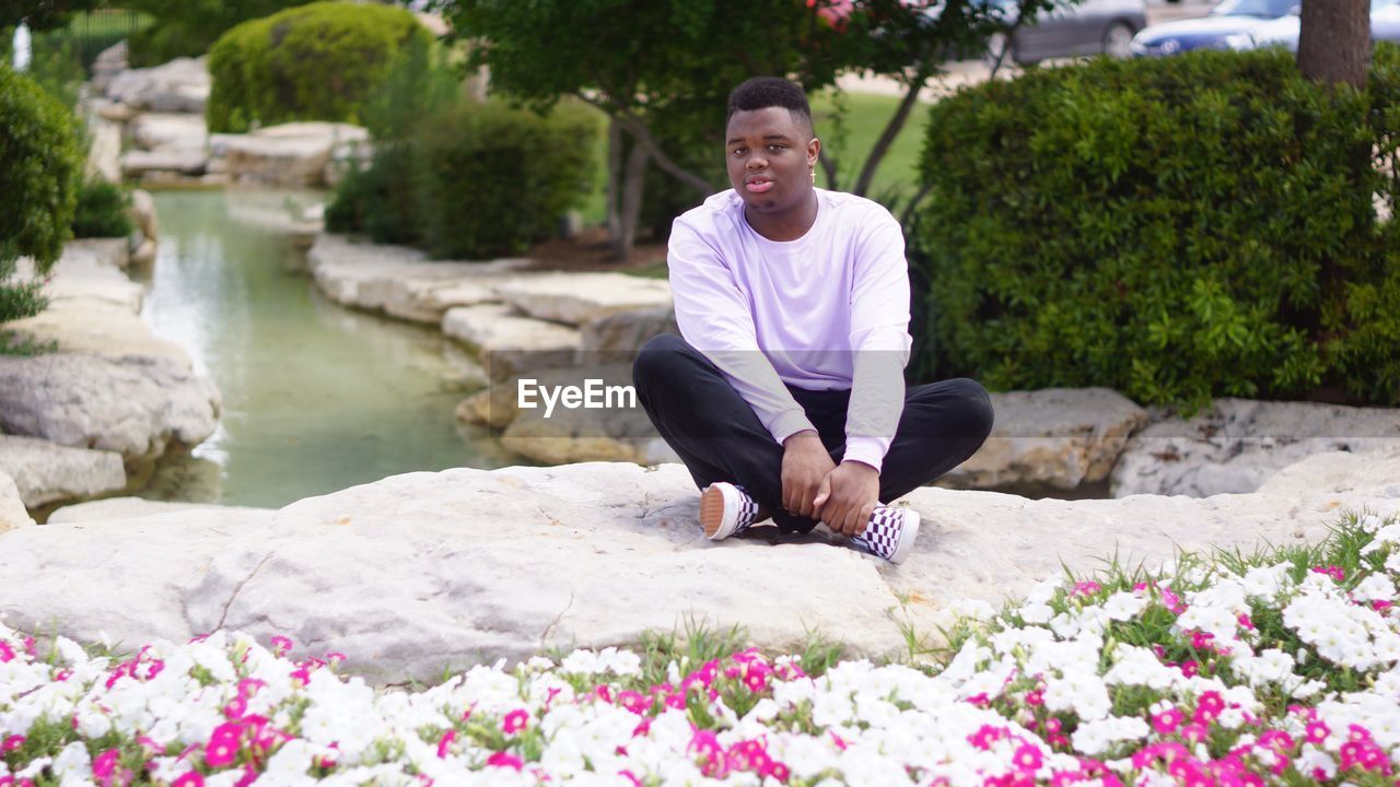 Full length portrait of young man sitting on rock against pond