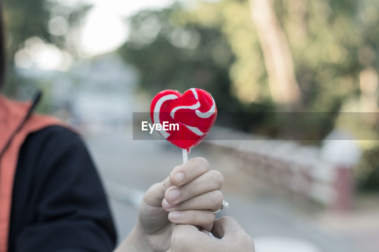 Midsection of person holding heart shape lollipop