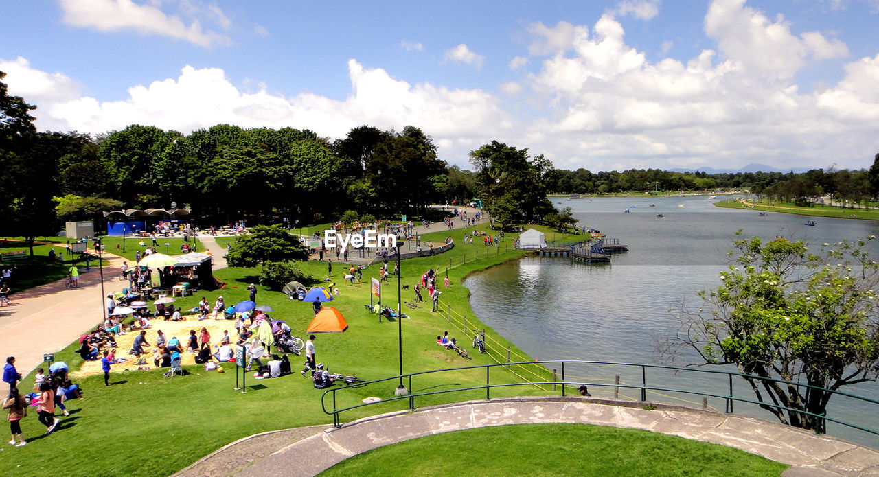 HIGH ANGLE VIEW OF PEOPLE RELAXING BY LAKE AGAINST SKY