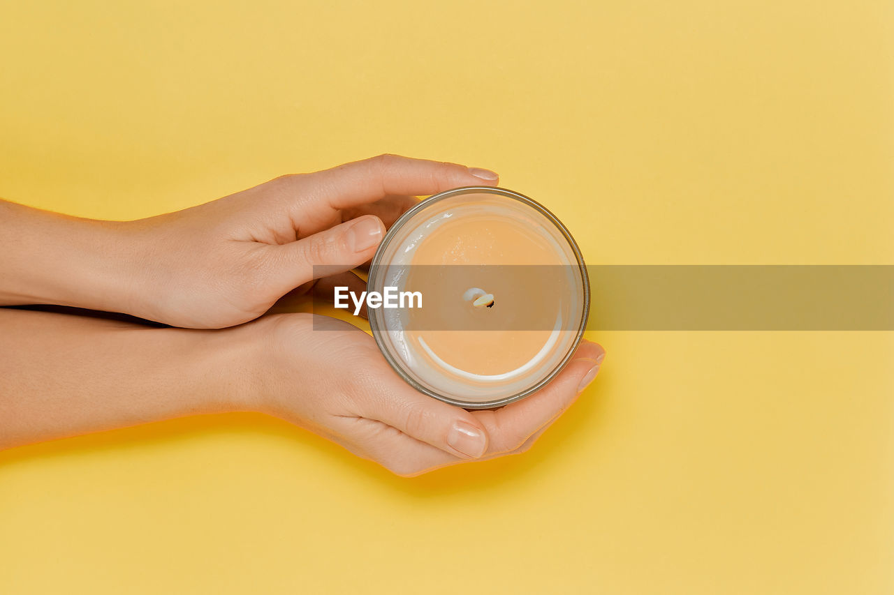 cropped hand of woman holding coffee cup against yellow background