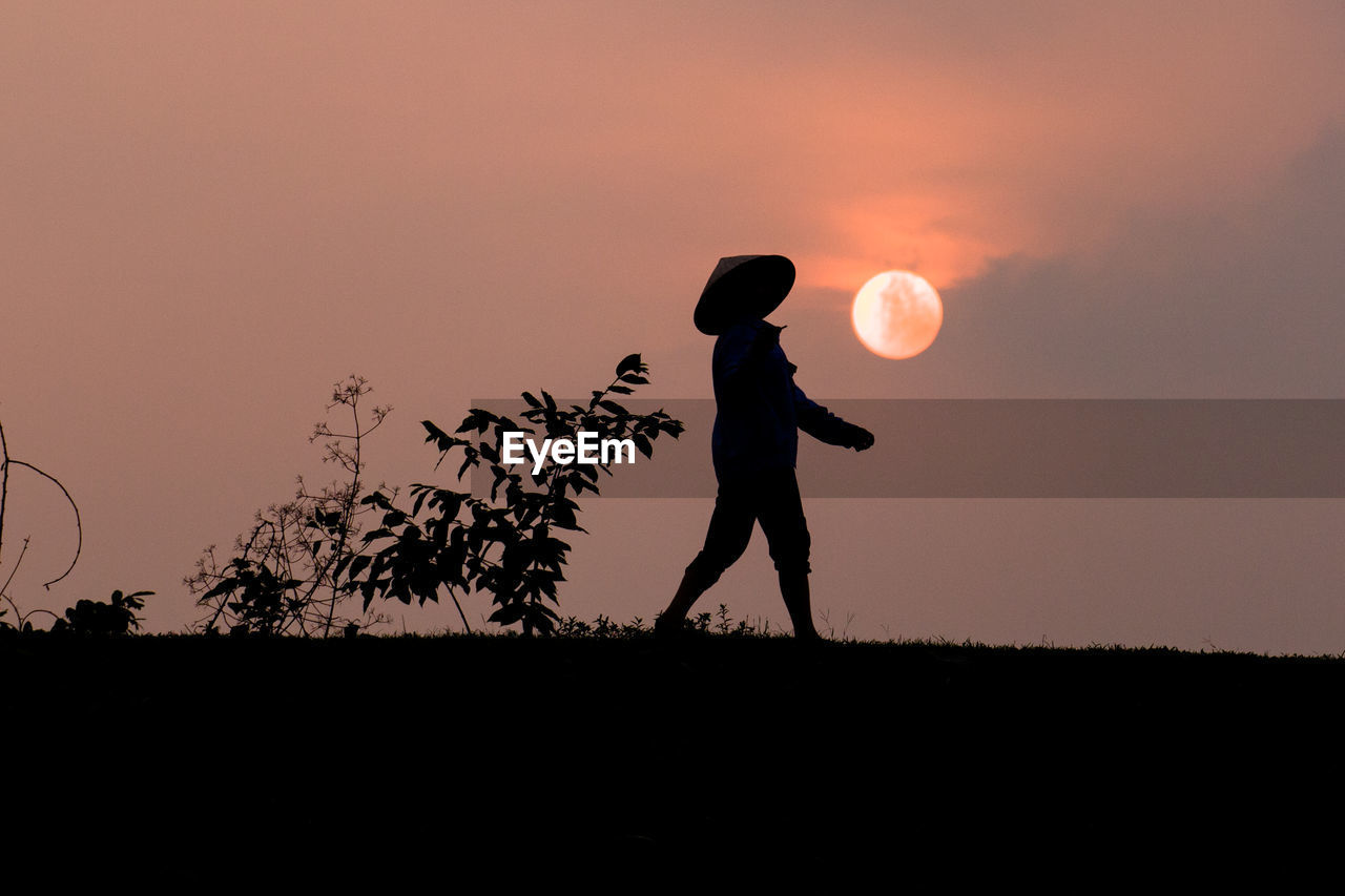 SILHOUETTE OF MAN STANDING ON FIELD AGAINST SKY