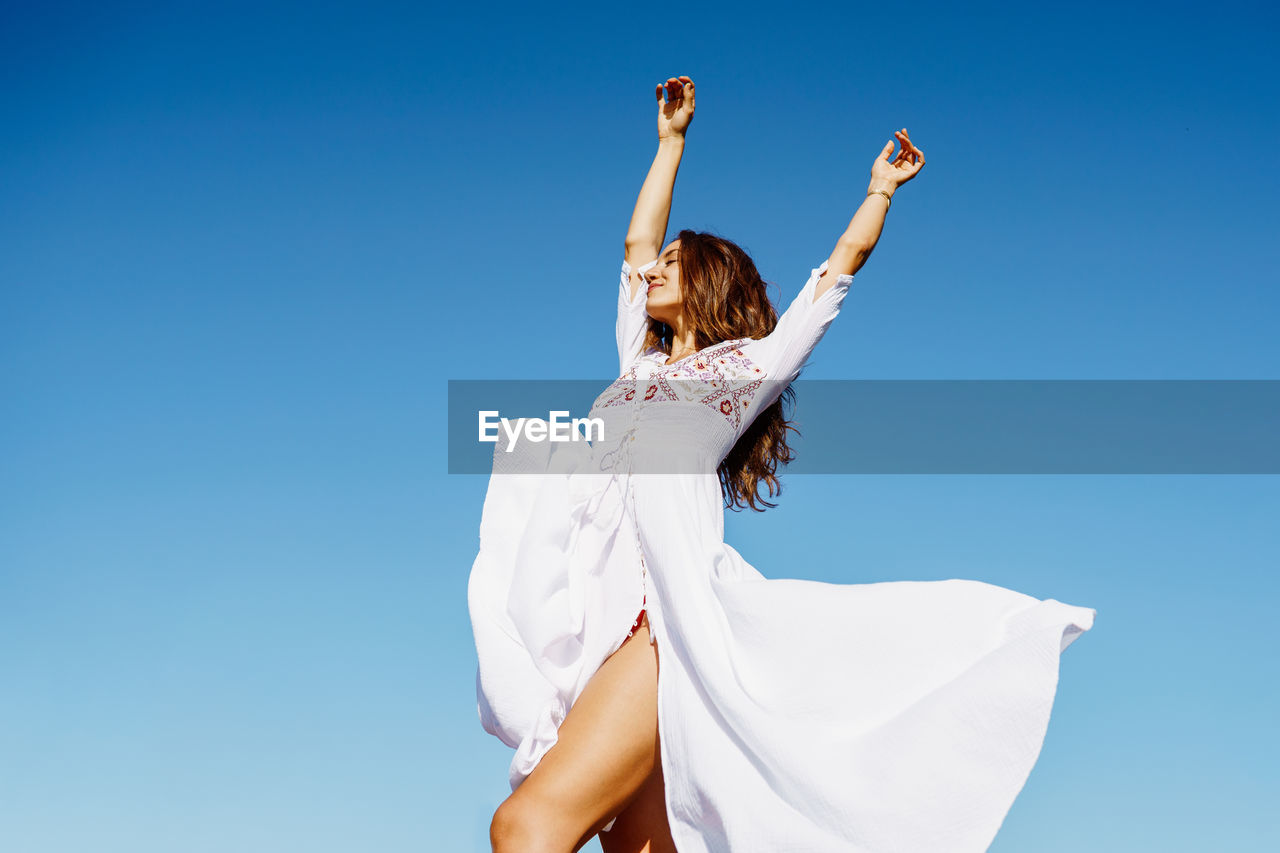 Low angle view of woman with arms raised against blue sky