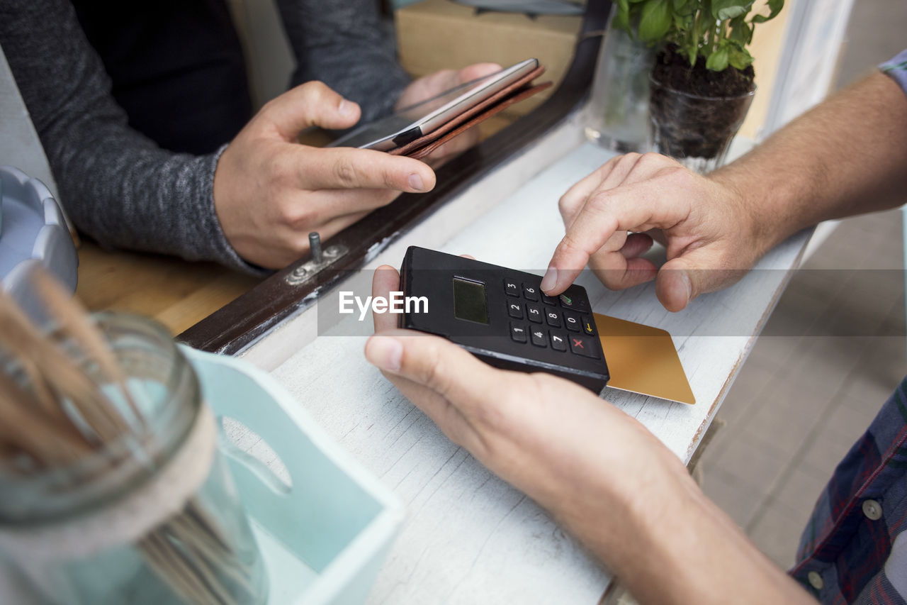 High angle view of customer paying through card reader while owner using digital tablet at food truck