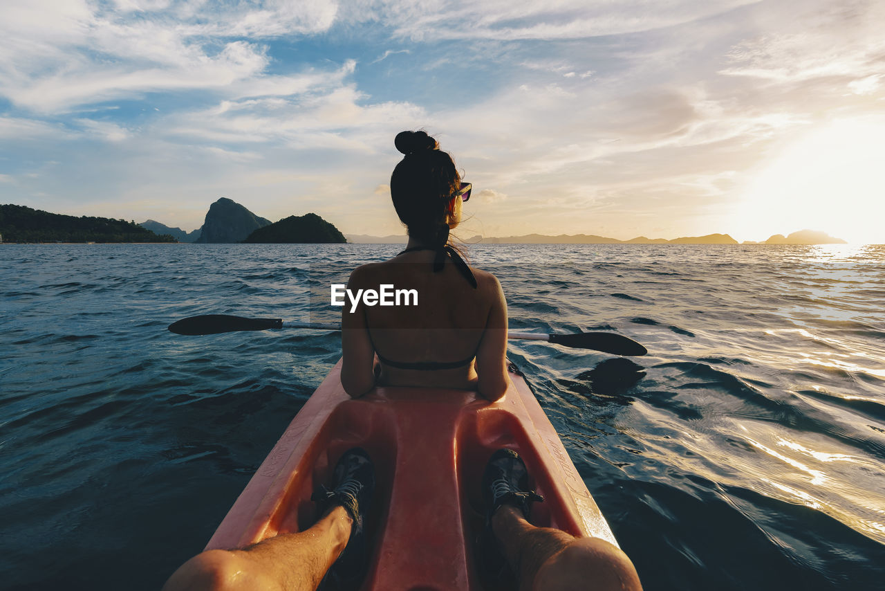 WOMAN STANDING ON SEA AGAINST SKY DURING SUNSET