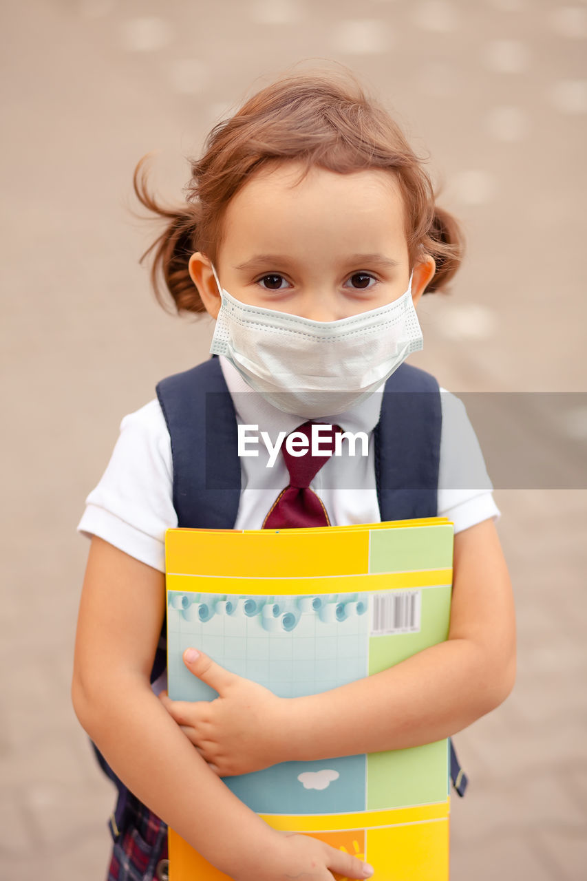 Portrait of girl wearing mask holding book standing outdoors