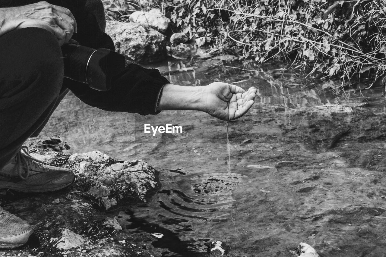Low section of photographer capturing water slipping from hand by river