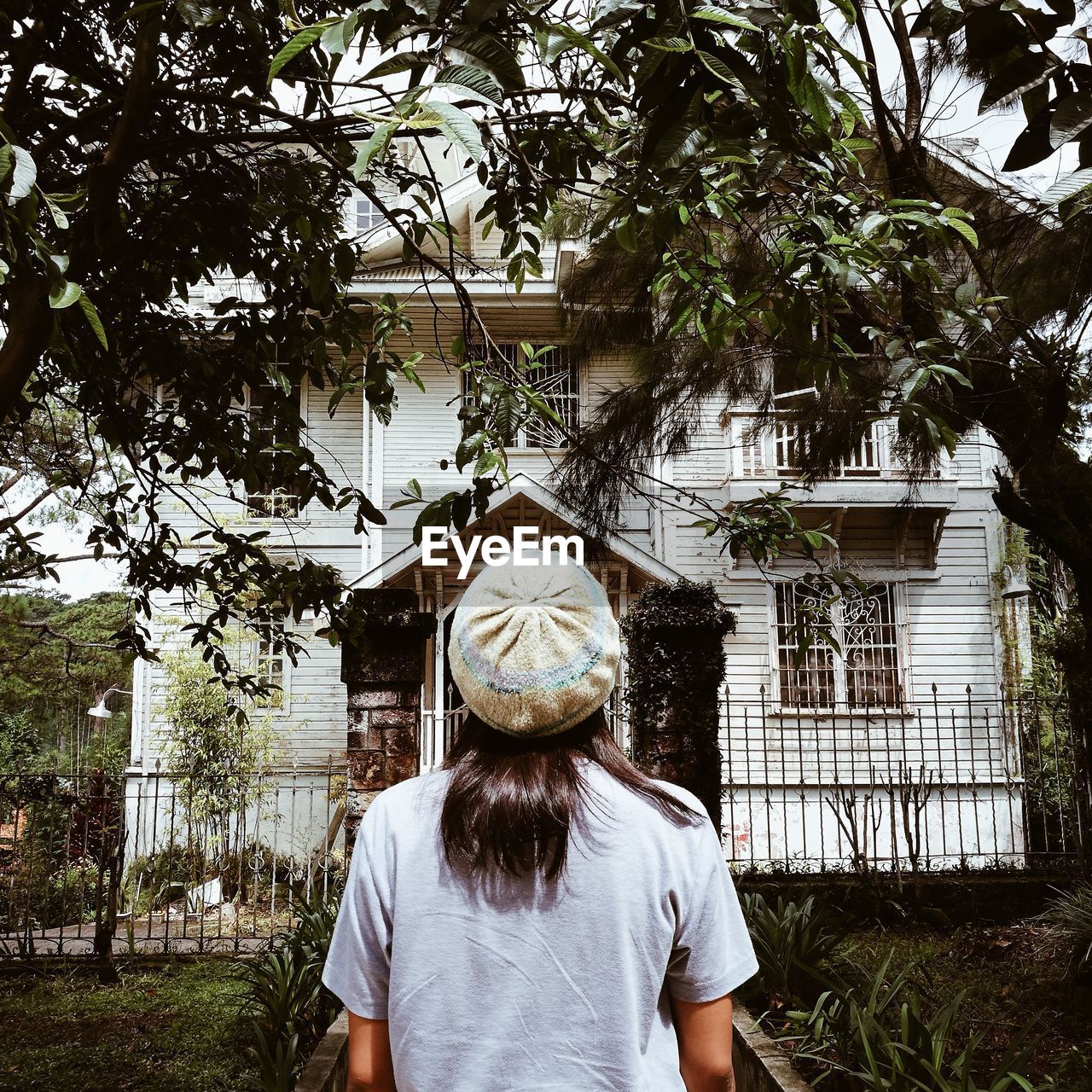 REAR VIEW OF WOMAN STANDING AGAINST TREE