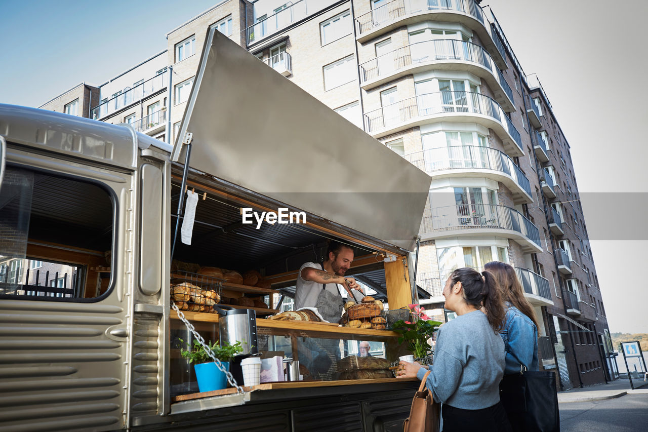 Female customers buying bread from salesman at food truck in city