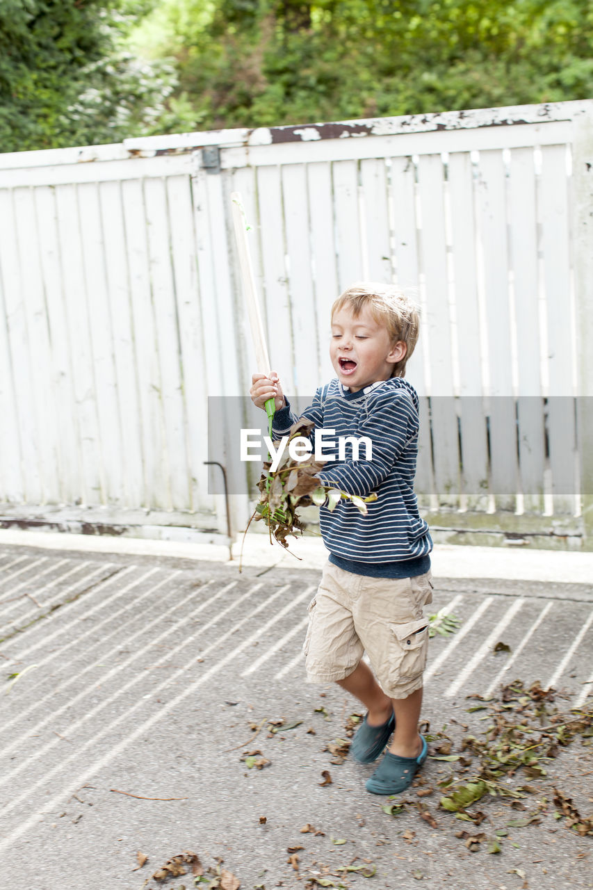 Smiling boy playing with fallen dry leaves at back yard