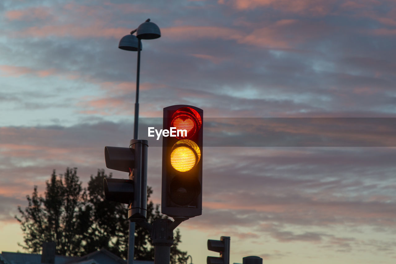 Low angle view of illuminated traffic signal against cloudy sky