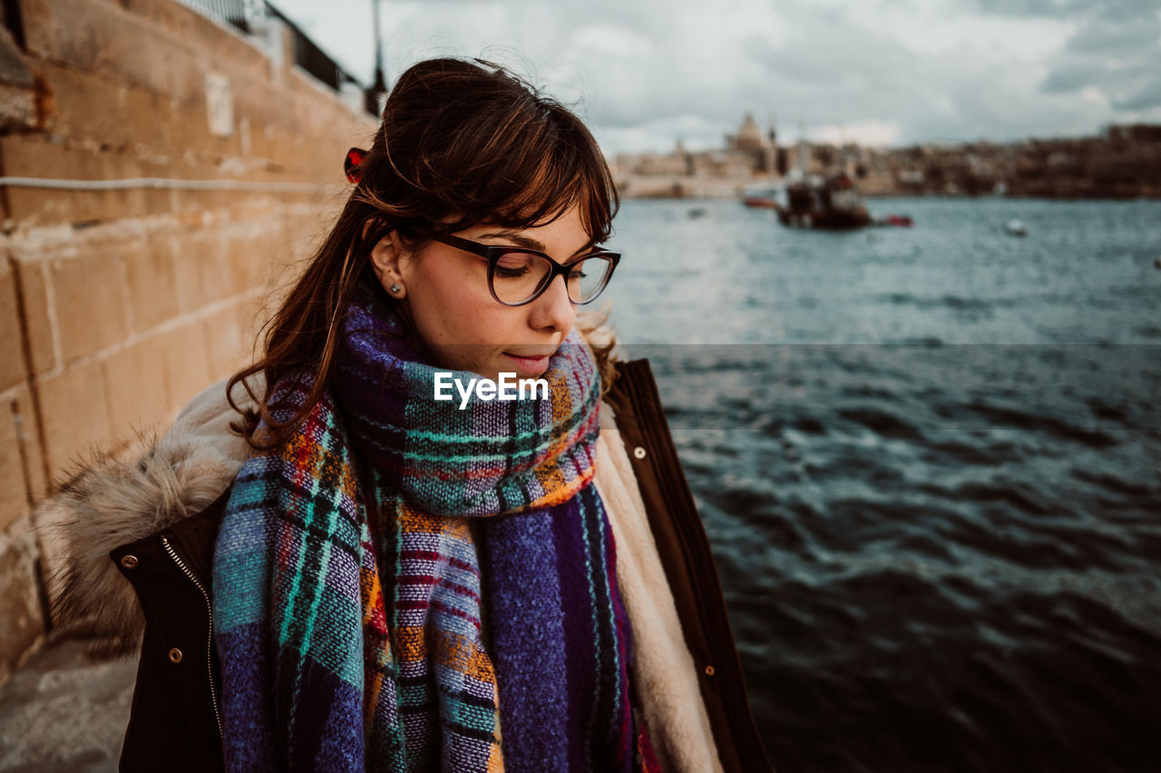 Close-up of woman wearing eyeglasses looking down standing by sea