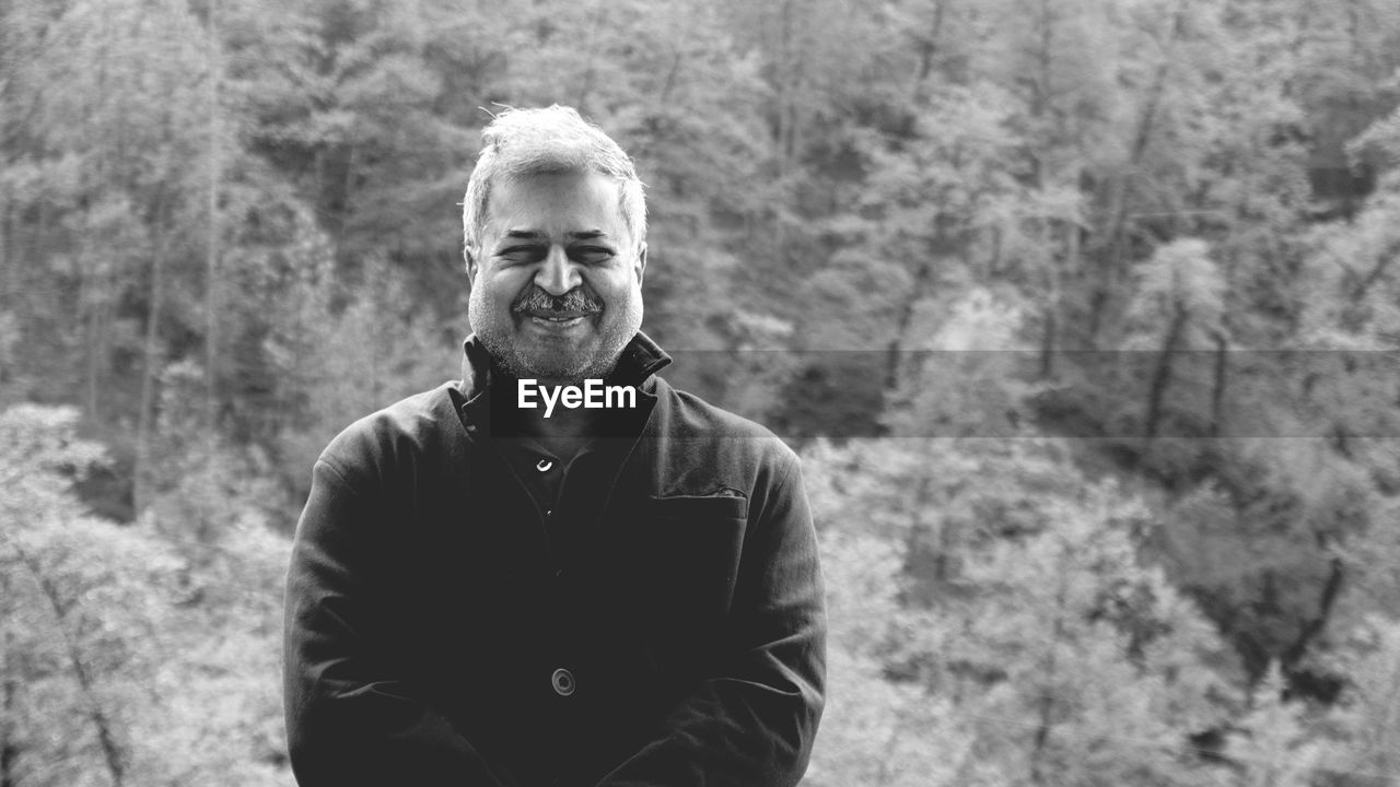 Portrait of man smiling while standing against trees