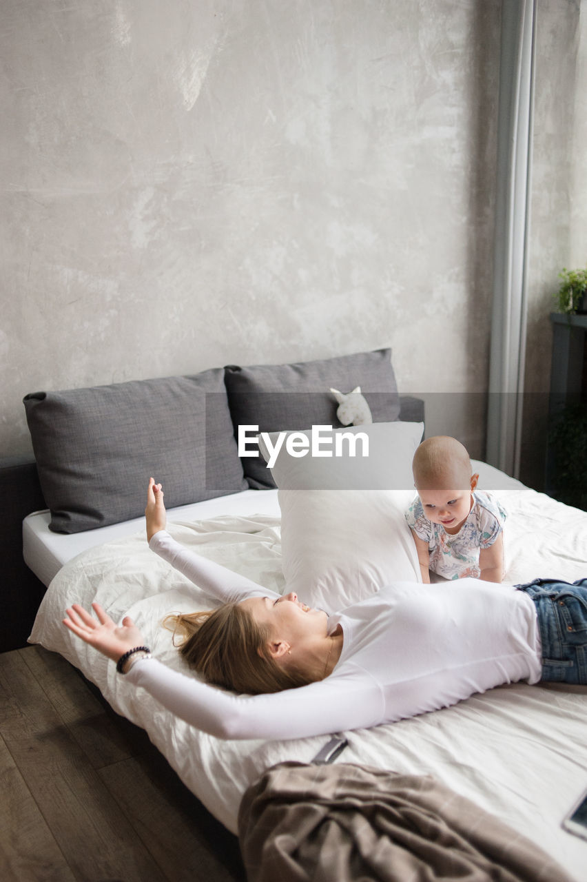 Adorable woman plays with child lying on bed, enjoying weekend indoors