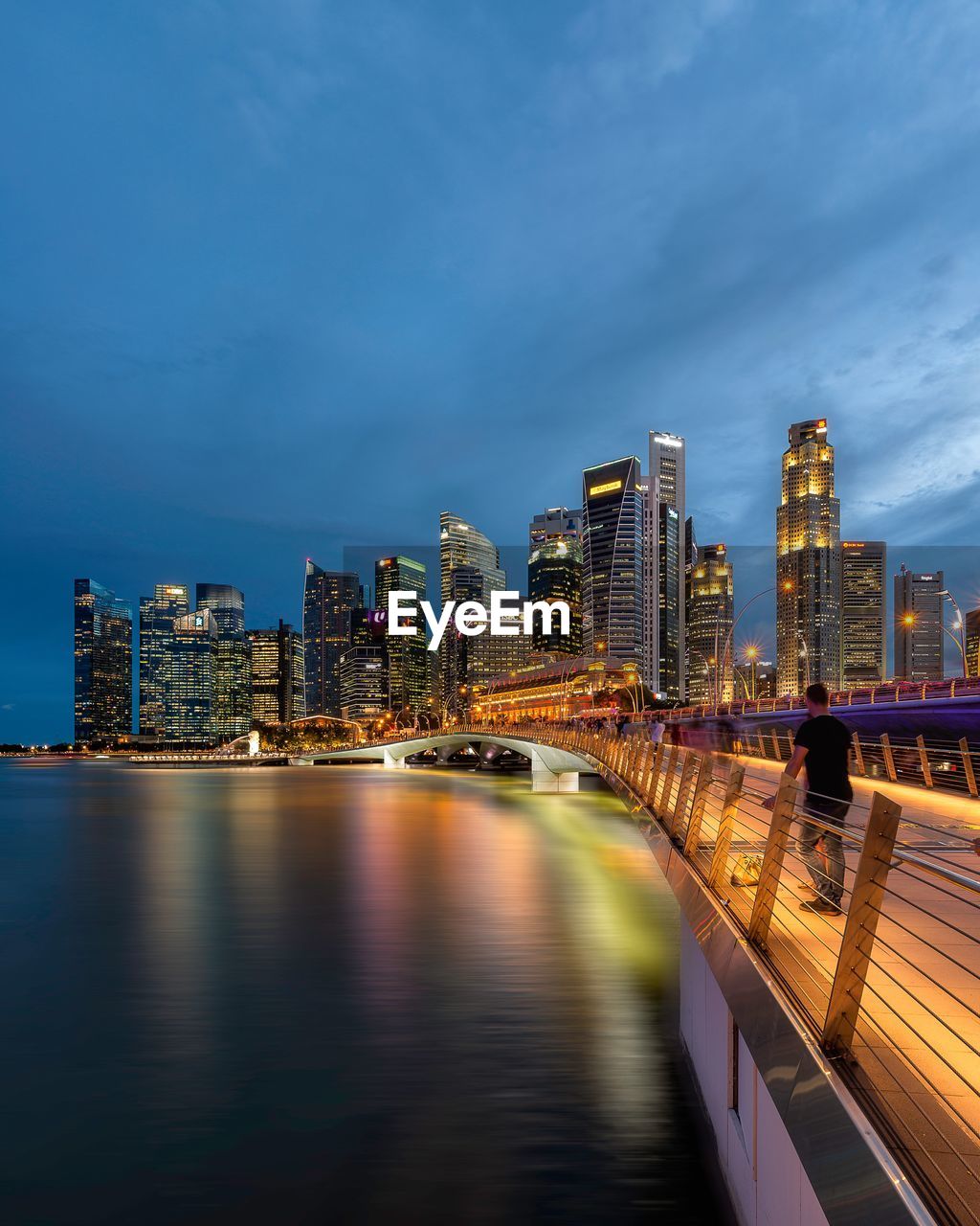 Illuminated buildings by river against sky in city