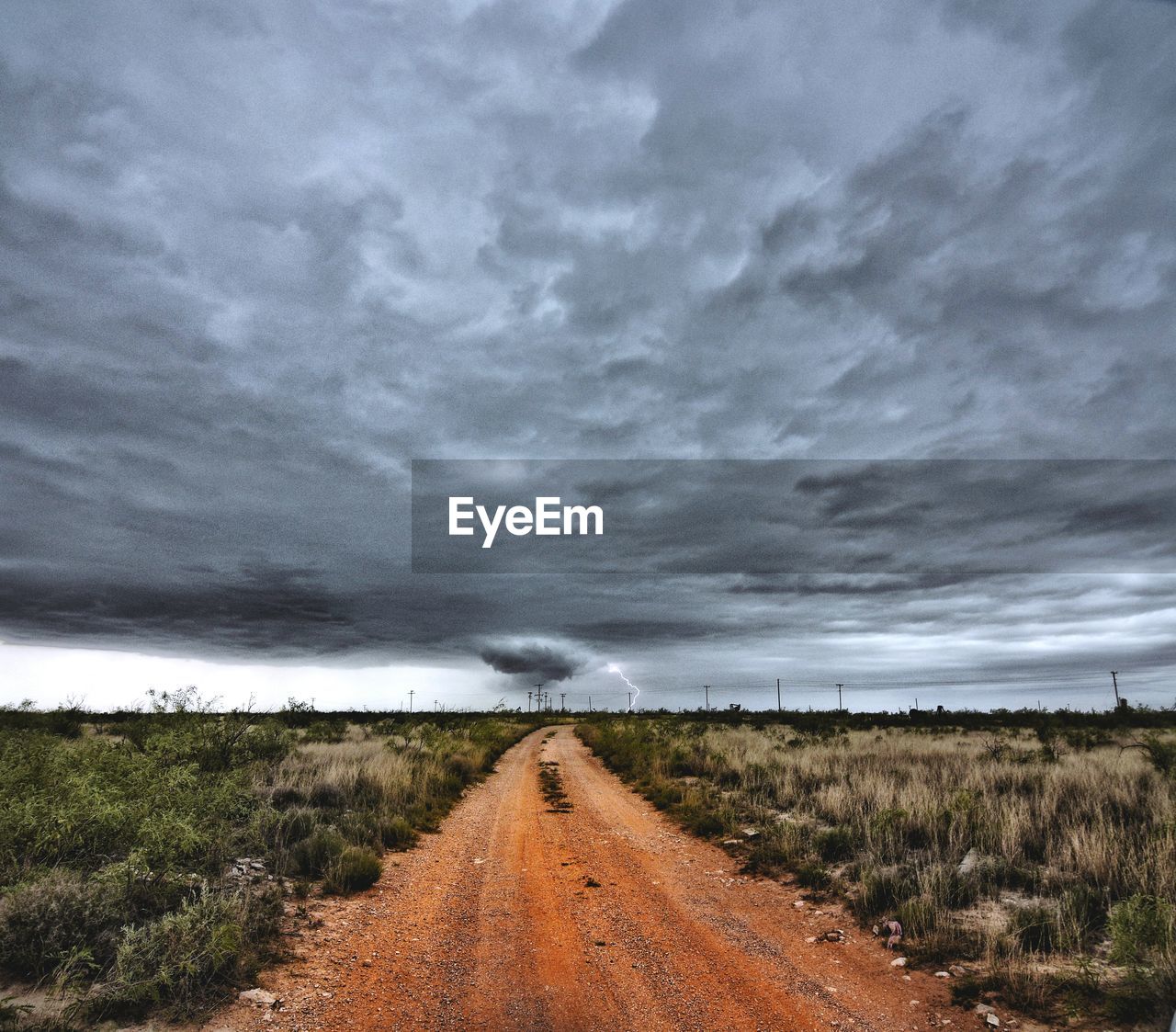 Footpath amidst grassy field against cloudy sky during storm