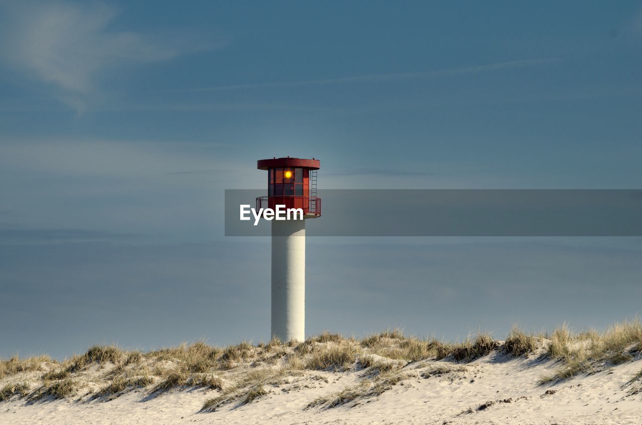 Lighthouse at beach against sky