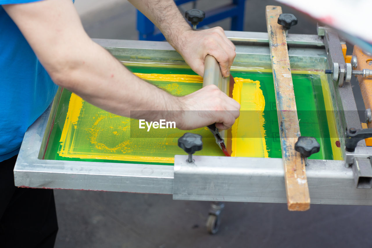 MIDSECTION OF MAN WORKING ON WOOD WITH YELLOW UMBRELLA