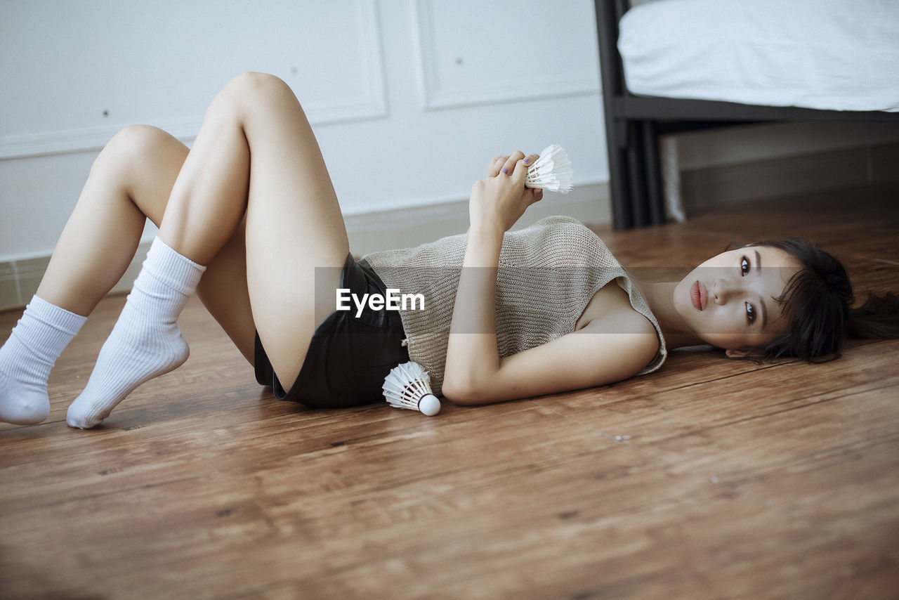 Portrait of woman lying on floor with shuttlecock at home
