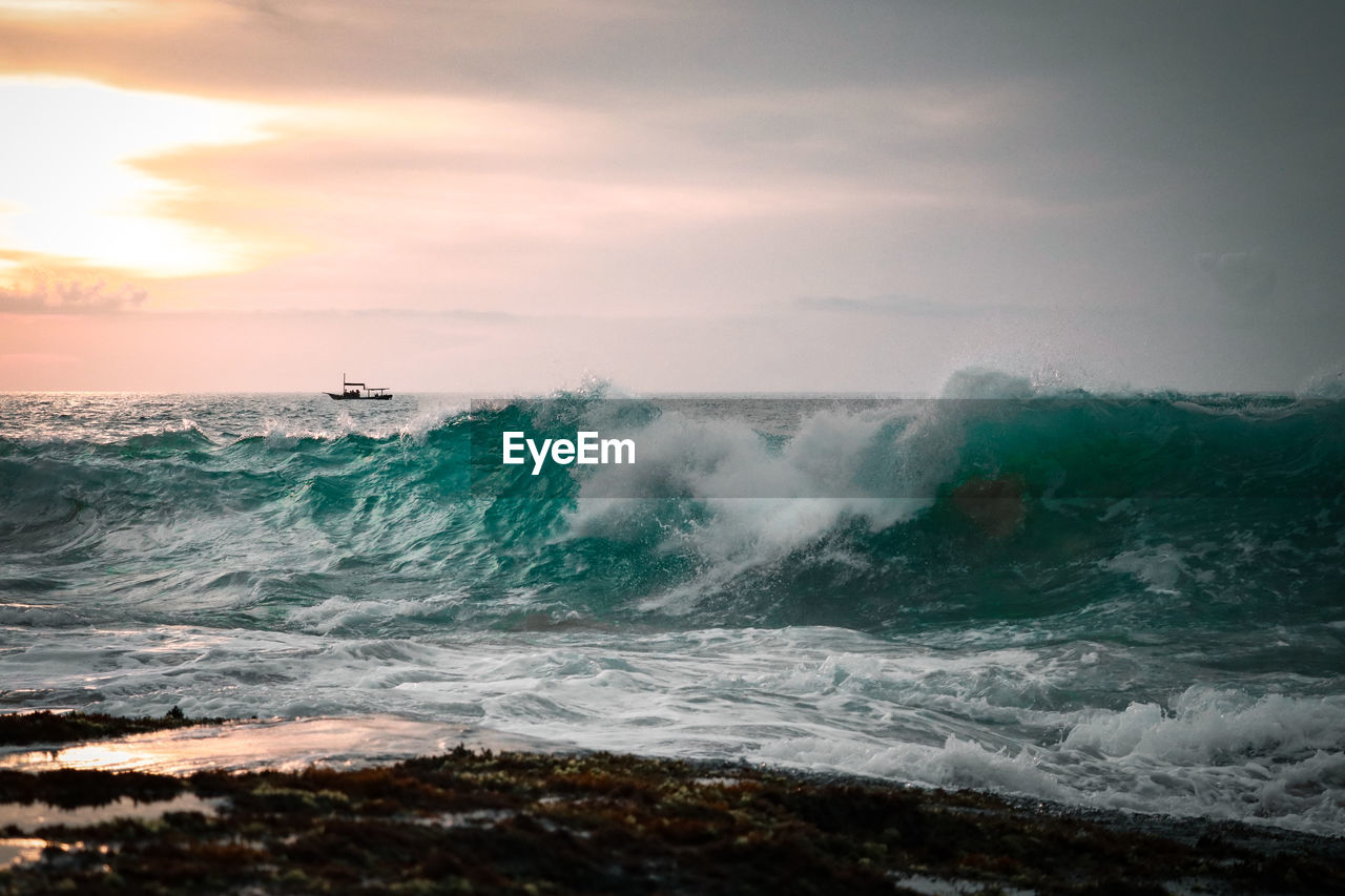 Waves splashing on shore against sky during sunset