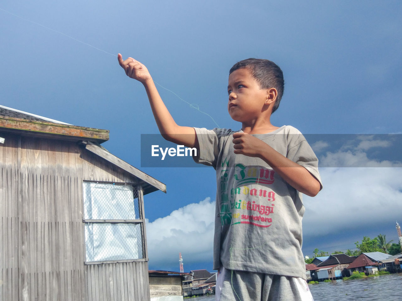Boy holding string while standing against blue sky