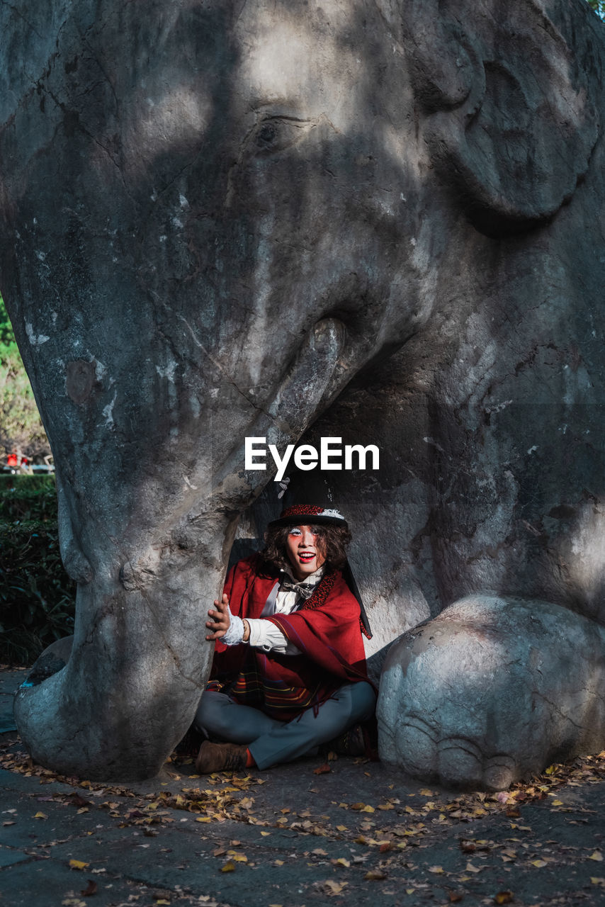 Man cosplaying mad hatter sitting under elephant statue