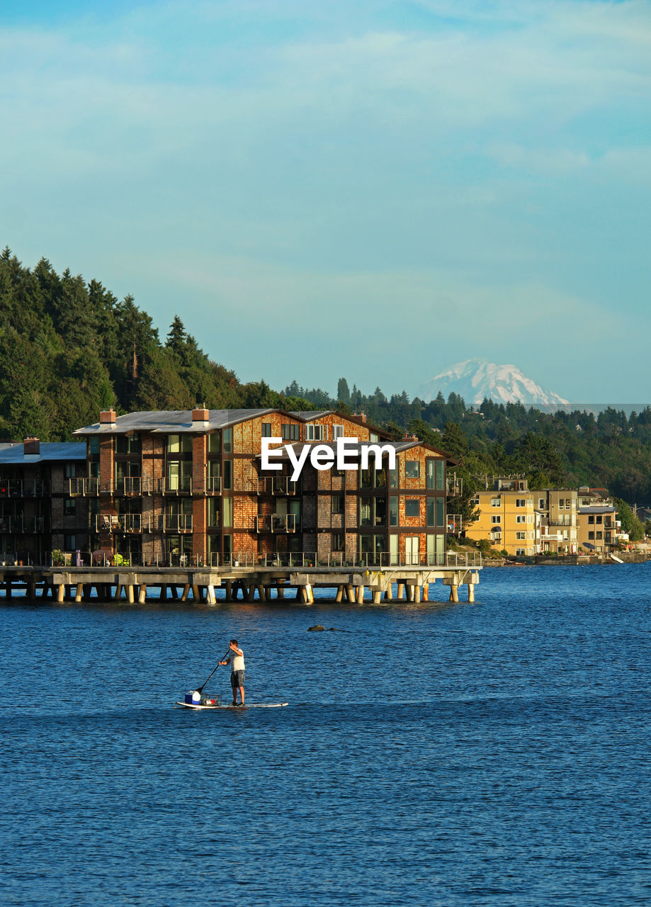 Man paddleboarding on lake with buildings in background