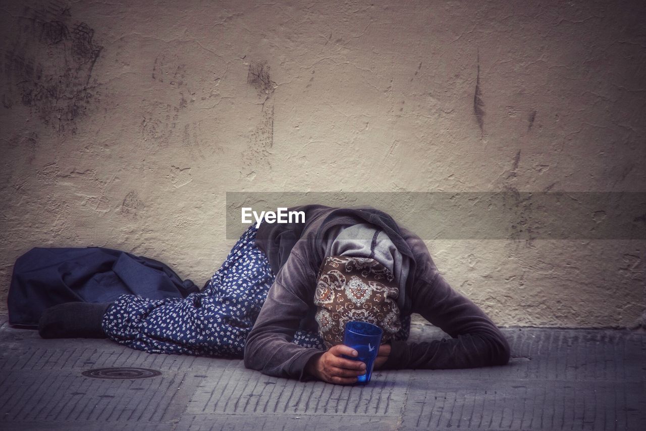 Beggar kneeling on sidewalk against wall