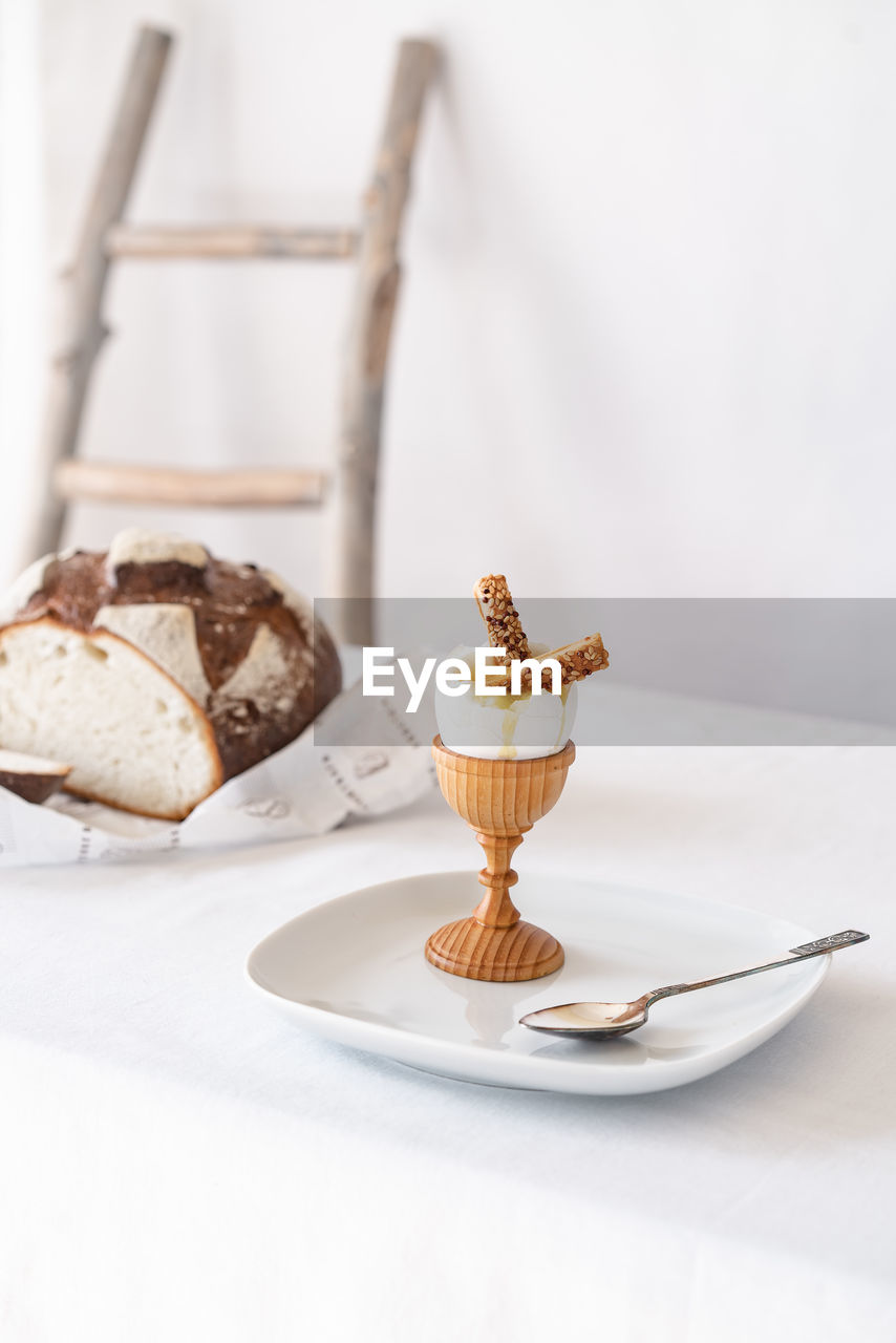 Two crackers with sesame seeds in a broken boiled egg on a wooden stand on a table with a white tablecloth