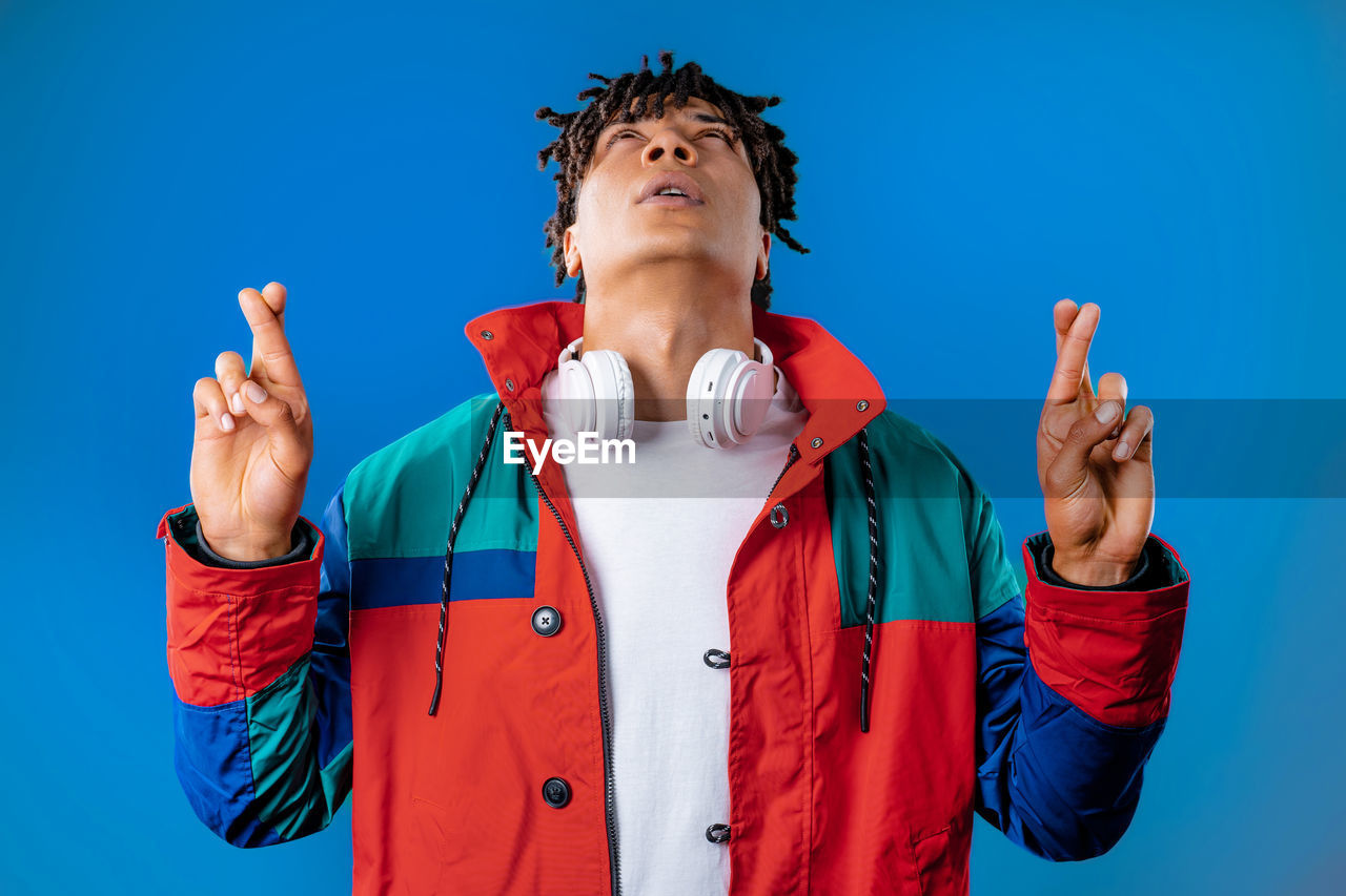 blue, one person, colored background, studio shot, adult, blue background, front view, gesturing, waist up, portrait, clothing, young adult, emotion, person, red, standing, hand, men, communication, indoors, technology, copy space, fun, humor, singing, sports, sign language