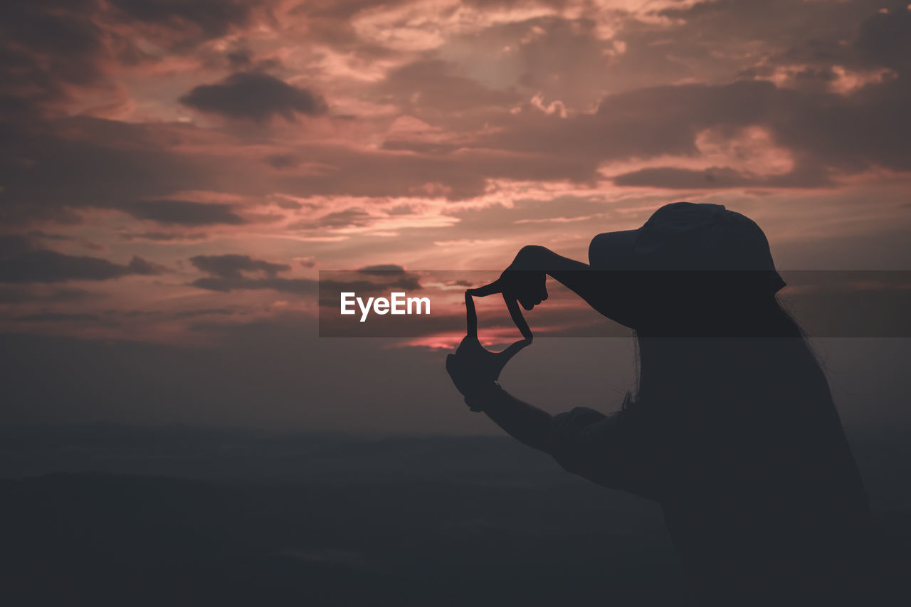 Silhouette of person photographing at sunset