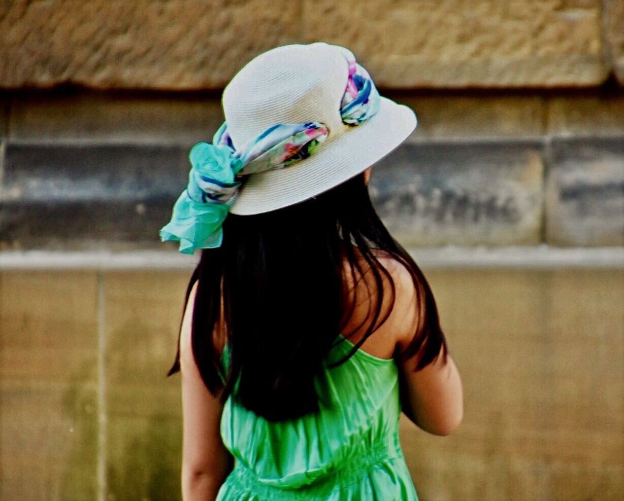 Rear view of girl wearing hat while standing against wall