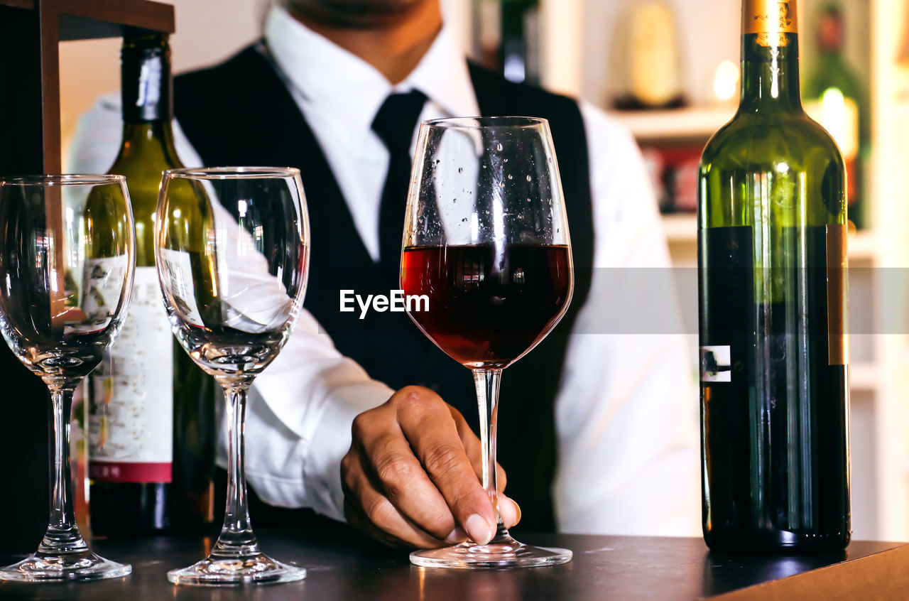 MIDSECTION OF MAN WITH WINE GLASS ON TABLE