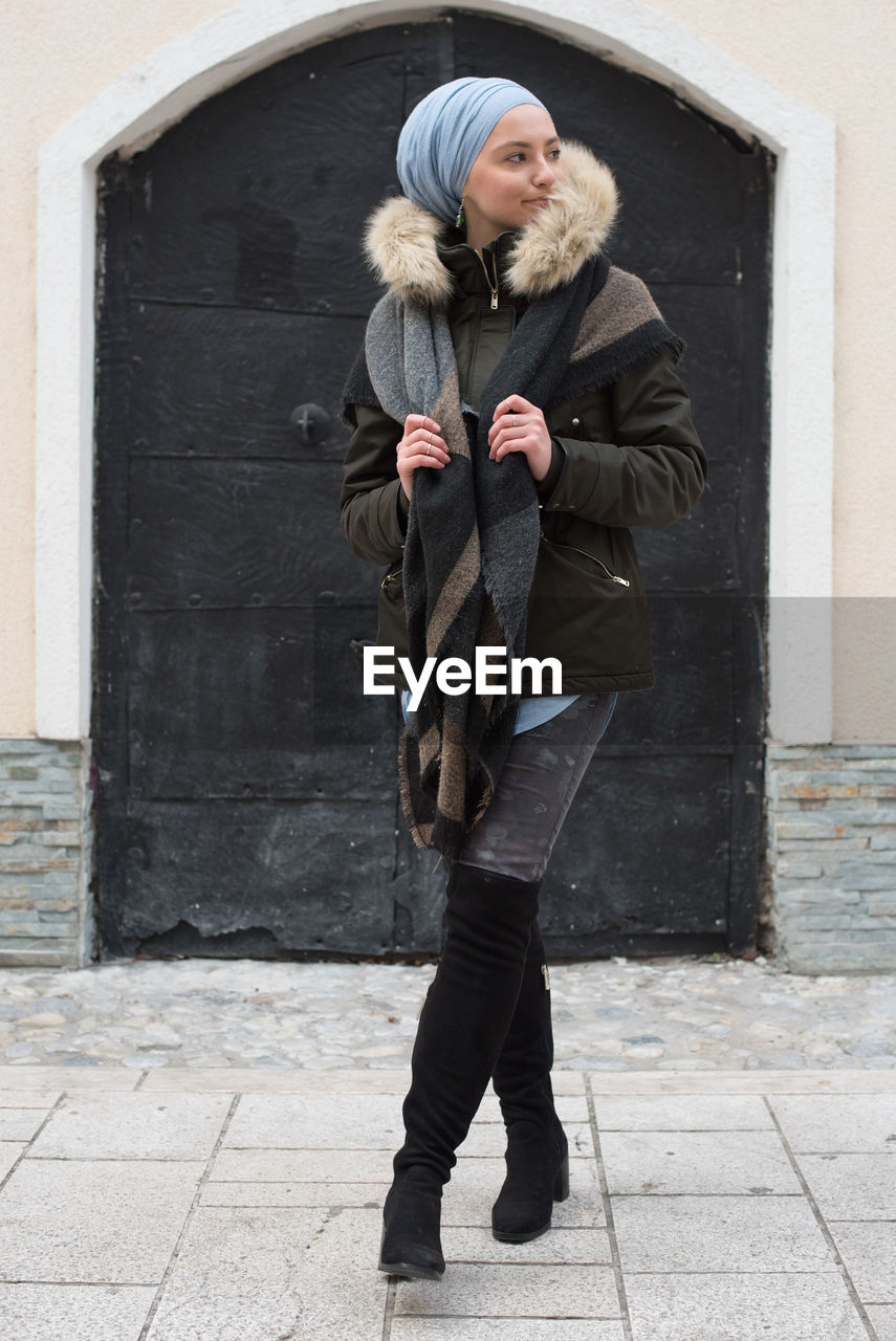 Woman looking away while standing against building