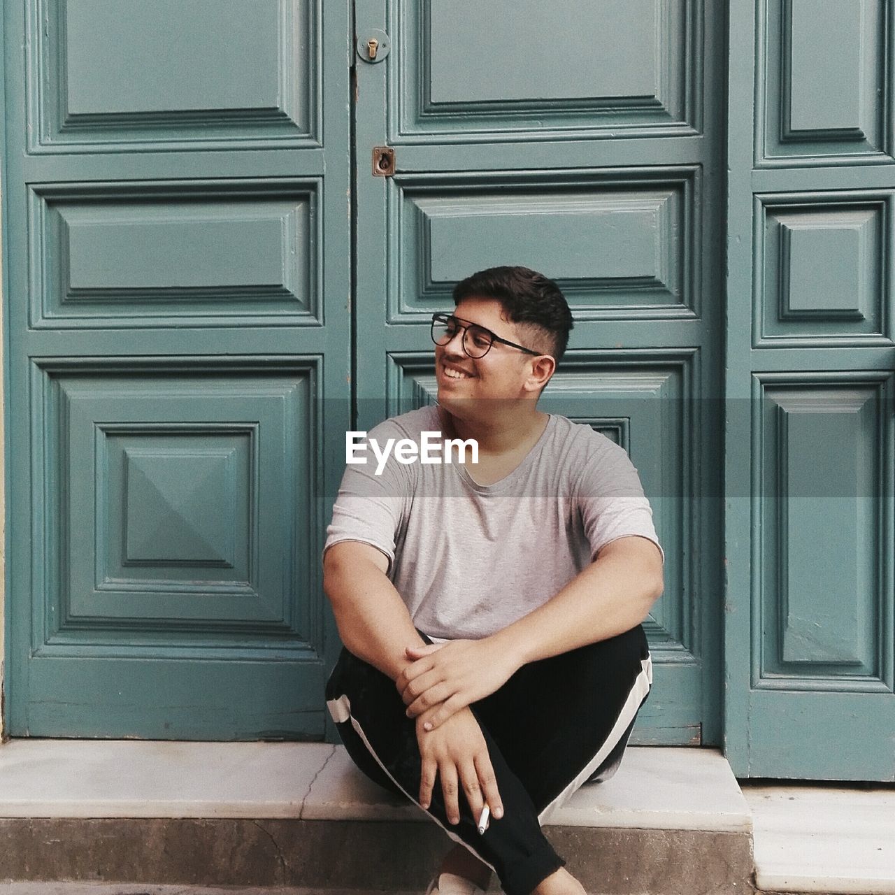 Smiling man sitting with cigarette against door