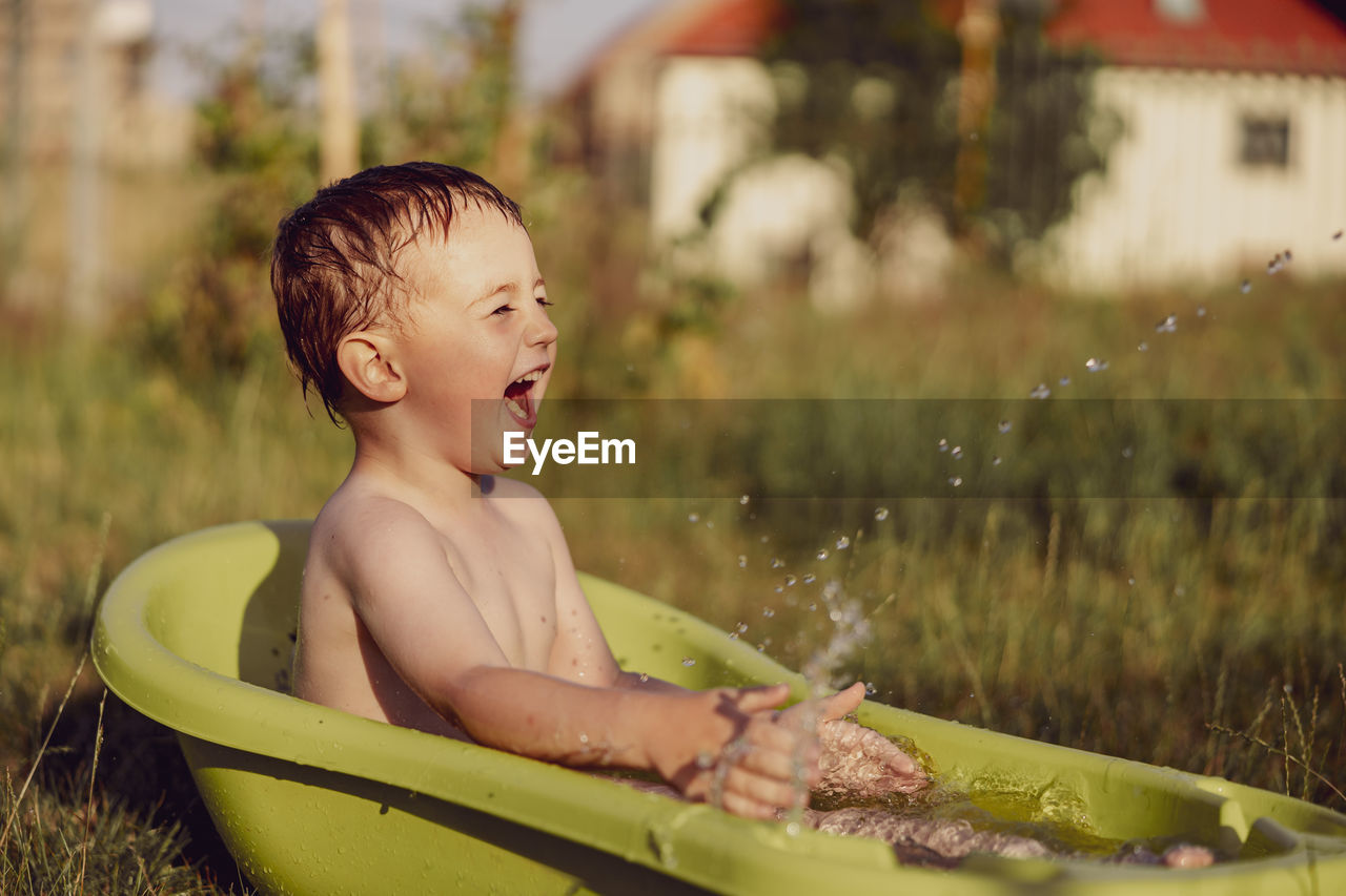 Cute little boy bathing in tub outdoors in garden. happy child is splashing, playing with water