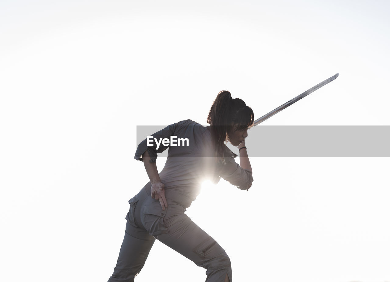 Young woman practicing martial arts with sword on sunny day