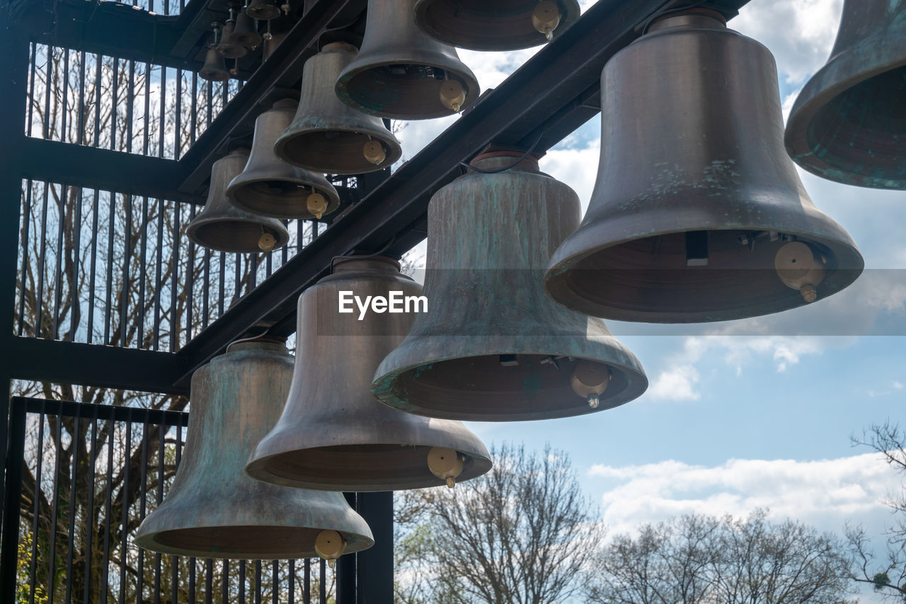 bell, low angle view, lighting, sky, church bell, no people, nature, tree, architecture, musical instrument, day, lighting equipment, light fixture, cloud, metal, plant, built structure, outdoors, hanging, street light, light, bare tree