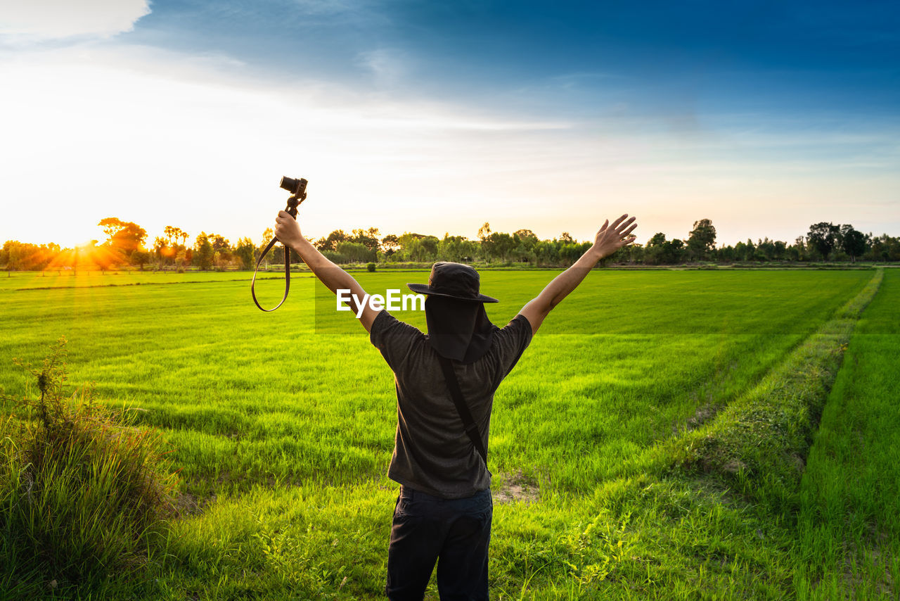 Rear view of man with arm raised standing on land against sky during sunset