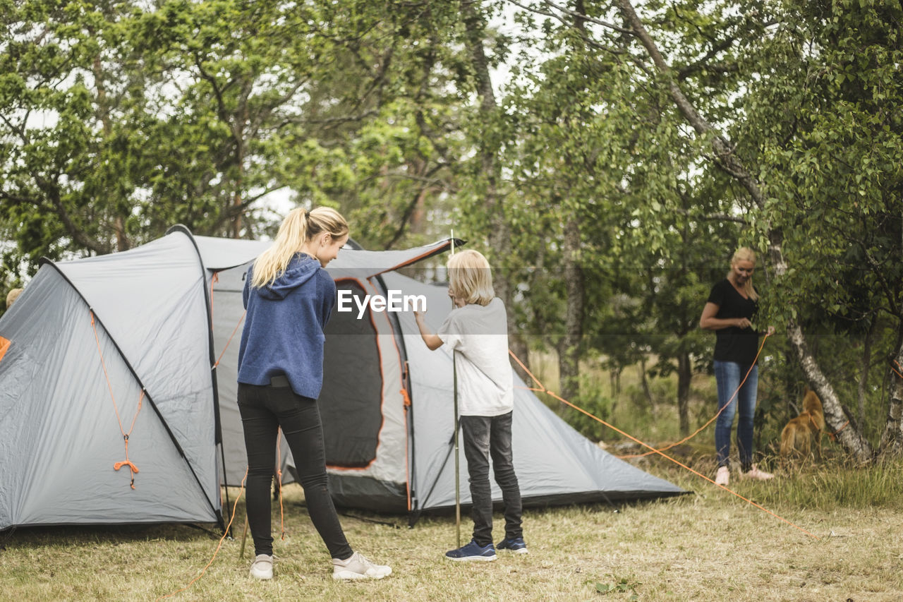 Siblings preparing tent in forest at camping site