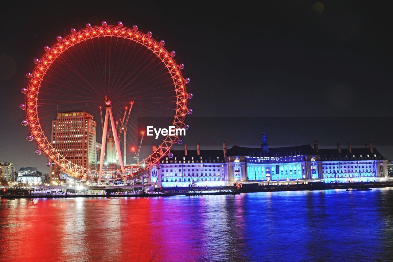 ILLUMINATED FERRIS WHEEL BY RIVER AGAINST SKY