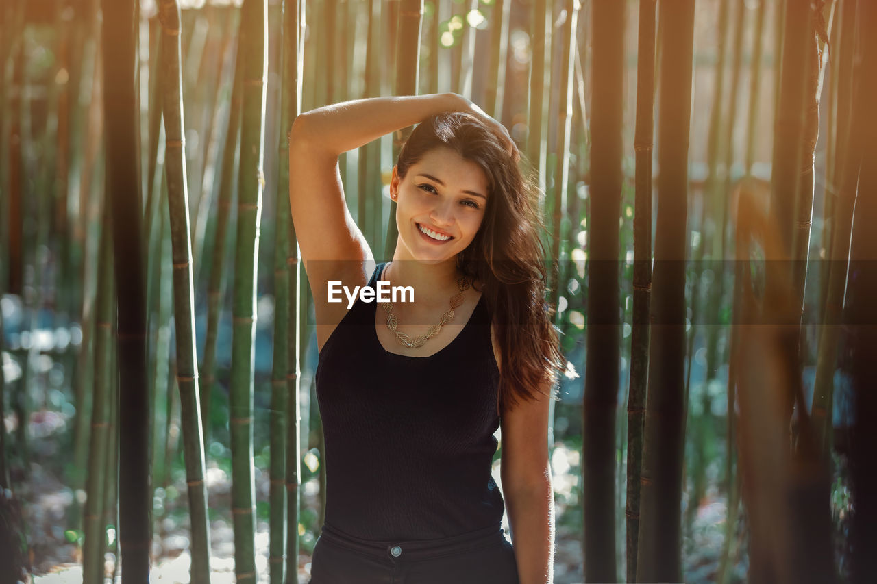 Young latina woman smiling at the camera, in front of bamboo and sunlight coming form the background