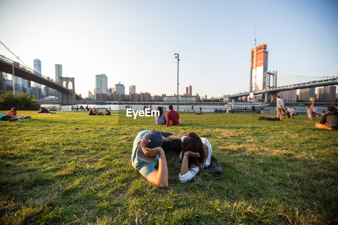 REAR VIEW OF PEOPLE IN PARK AGAINST CITYSCAPE