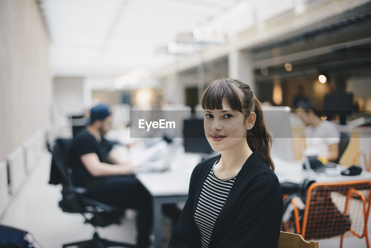 Portrait of confident computer programmer at office with colleagues working in background