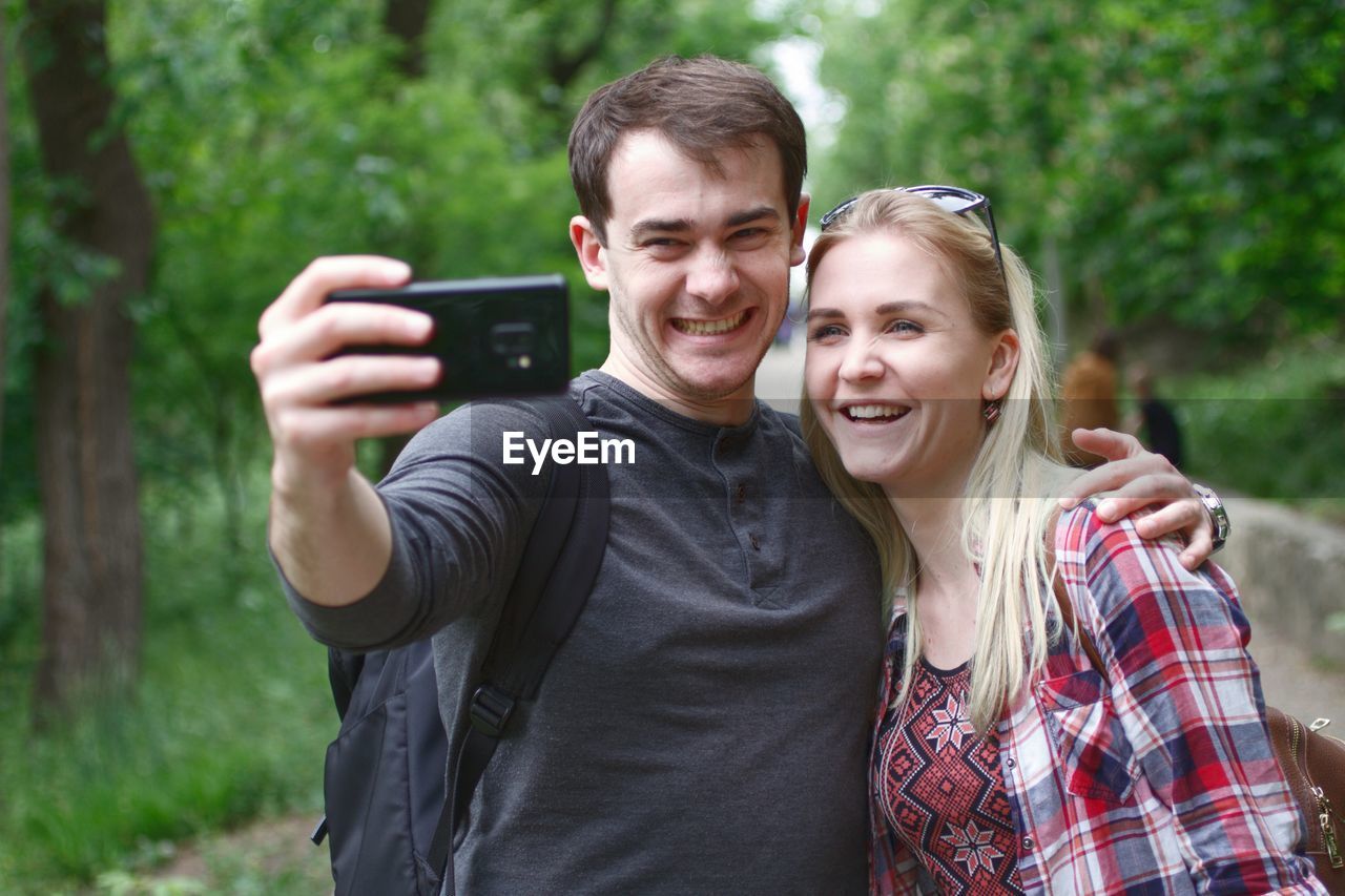 Happy friends taking selfie with smart phone at public park