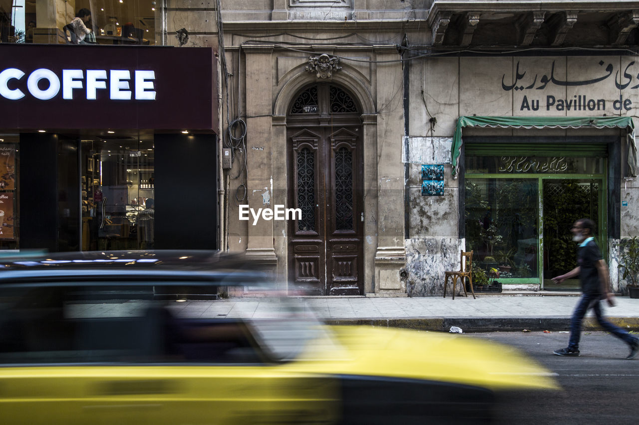 BLURRED MOTION OF BUS ON ROAD BY BUILDING