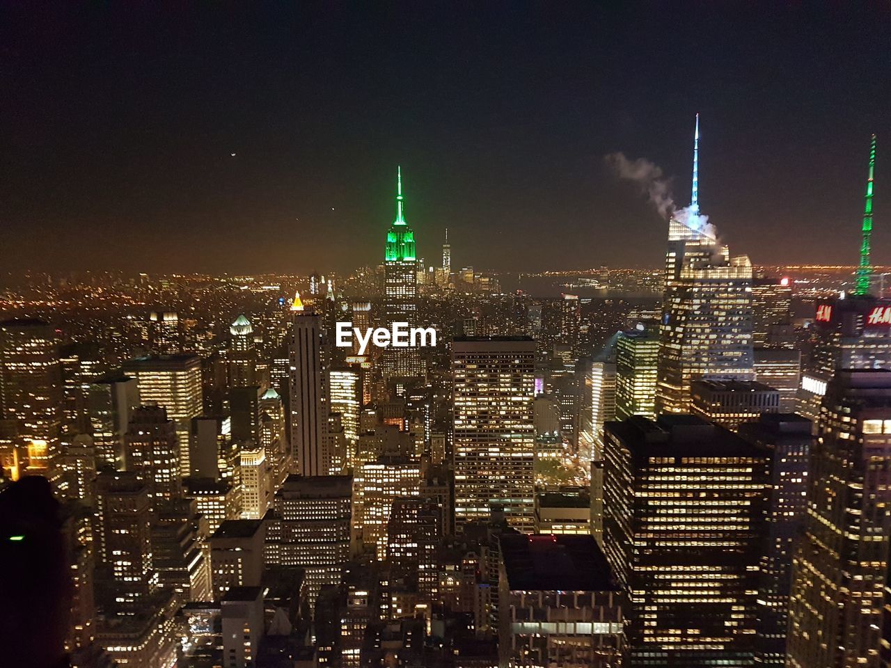 Empire state building amidst illuminated cityscape against blue sky at dusk