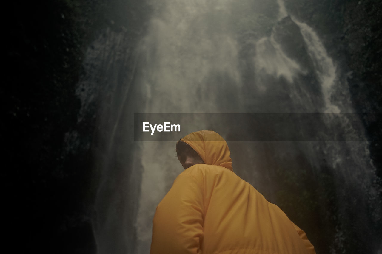 Rear view of man standing against yellow waterfall