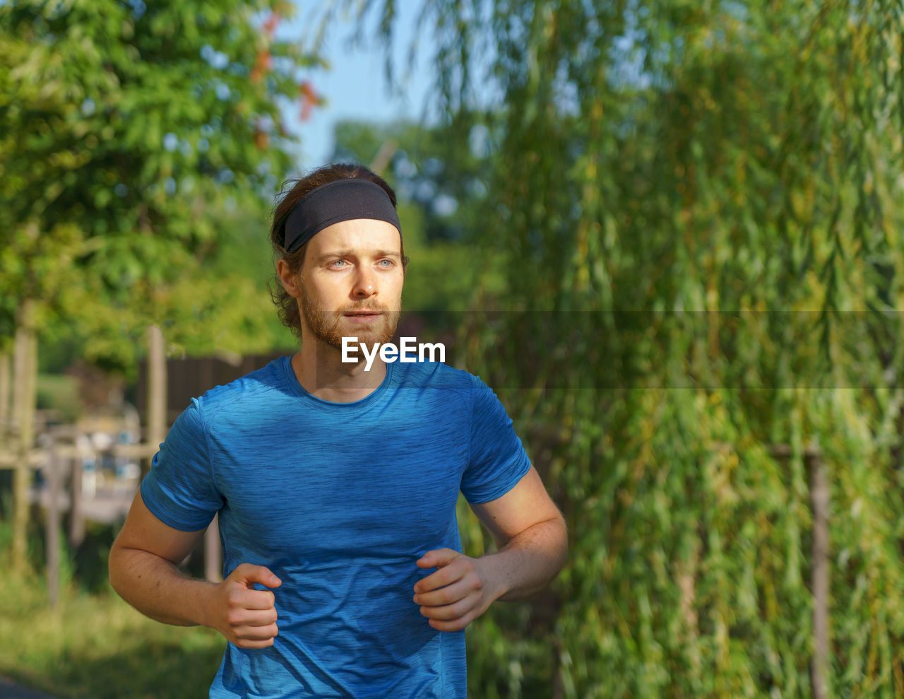 Athletic european man in sportswear jogging on road in green park on beautiful summer day